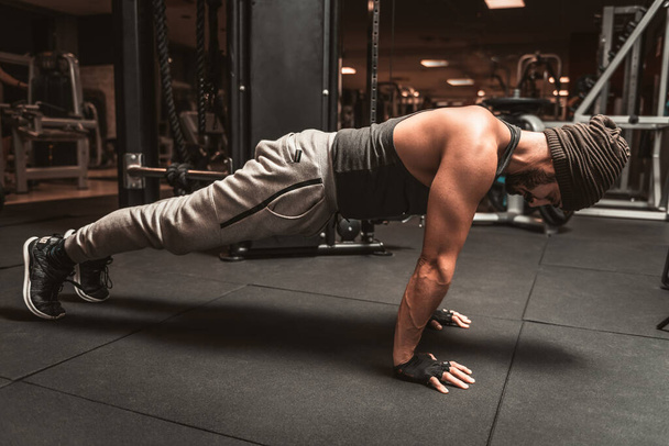 Un homme sportif dans la salle de gym fait des exercices de yoga, pratique debout dans la pose de planche, faire des exercices push up ou push up, entraînement, couvert pour toute la longueur. - Photo, image