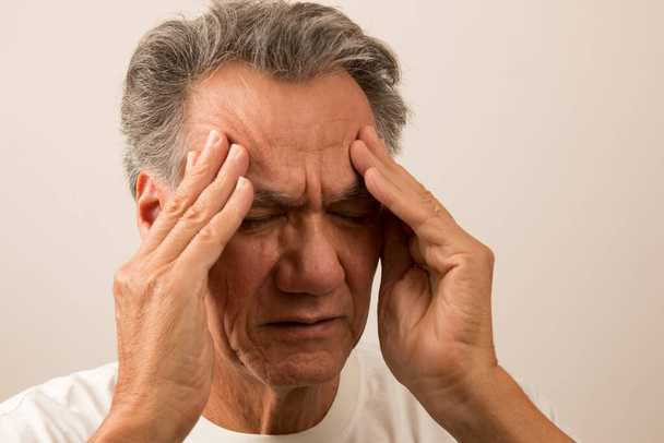 Starší muž v bolestech z bolesti hlavy si třel spánky, aby se mu ulevilo  - Fotografie, Obrázek