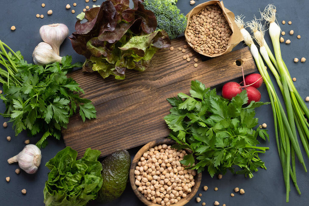 Groene groenten en linzen en kikkererwten liggen rond een rustieke houten snijplank. Plaats voor tekst. Gezond biologisch voedsel koken in de keuken thuis. Salade Ingrediënten - Foto, afbeelding