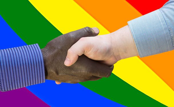Mustien elämillä on väliä. Lähikuva kuva kädenpuristus välillä afroamerikkalainen ja eurooppalainen käsissä. Kädenpuristus LGBT-lipun edessä. - Valokuva, kuva