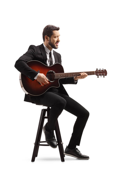 Musician with an electric guitar sitting on a chair and playing isolated on white background - Foto, immagini