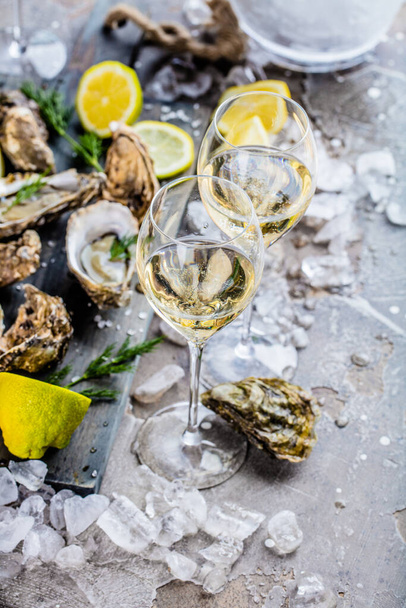 gourmet oysters with ice cubes, lemons and wine glasses on grey surface    - Фото, изображение