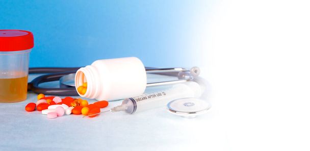 Die Nahaufnahme leerer Urinbehälter für Test, Spritze, Phonedoskop und farbige Pillen auf blauem Hintergrund - Foto, Bild