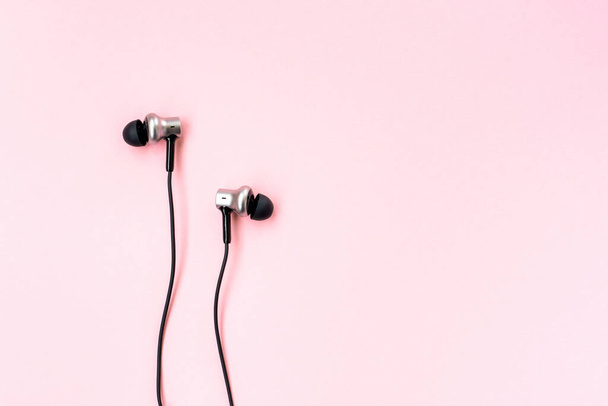 Black music earphones for smartphone on a pink pastel background. Minimalist flat lay. Empty place for writing. Copy space. Top closeup view.  - Photo, Image