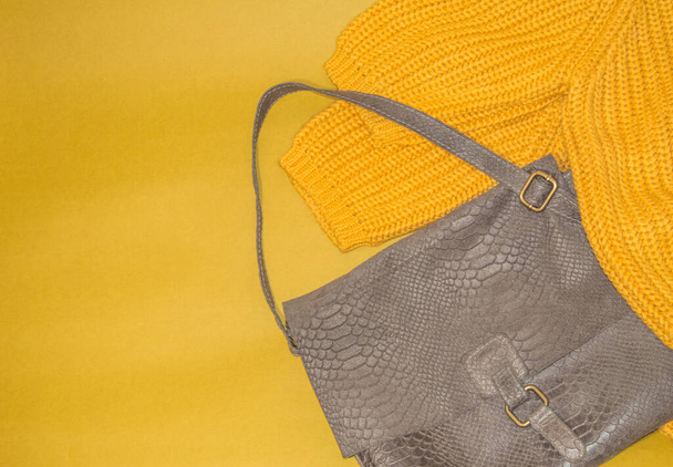 Ein gelber Strickpullover in Übergröße und eine luxuriöse graubraune Ledertasche auf gelbem Hintergrund. Draufsicht auf die Freizeitbekleidung von Frauen. Herbst und Winter Kollektion von Kleidung und Accessoires. - Foto, Bild