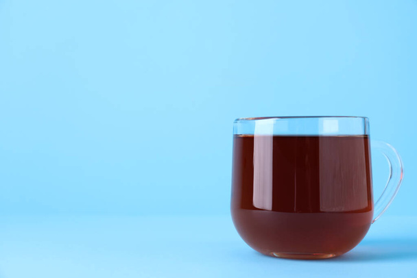 Glass cup of aromatic black tea on light blue background, space for text - Fotografie, Obrázek