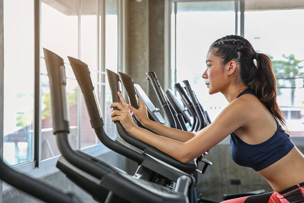 The female is cycling in the gym. Portrait of girl exercising on cardio machines in the sport club. Pretty women body builder working out at the gym. asian people. - Photo, Image