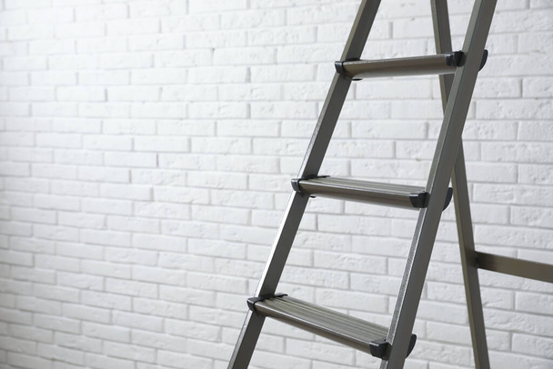 Metal stepladder near white brick wall, closeup. Space for text - Photo, image