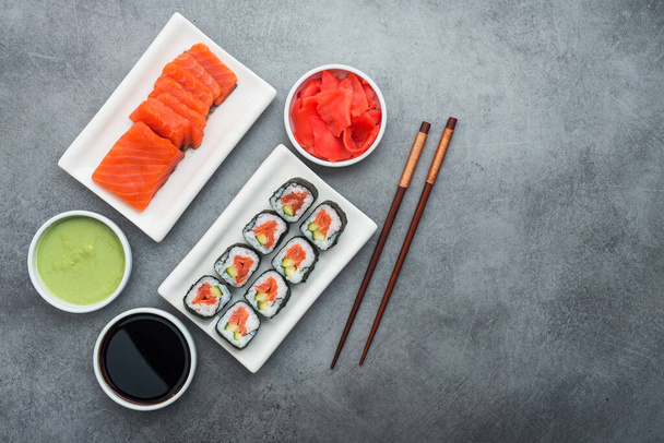 Szusi, lazac, gyömbér, wasabi és evőpálcika hozzávalókkal, kő alapon. ízletes japán étel - Fotó, kép