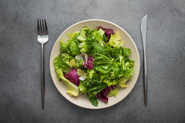 石のテーブルの上にレタスとアルグラと新鮮な緑のサラダミックス.食事の概念の背景。ビーガンフード。トップビュー - 写真・画像