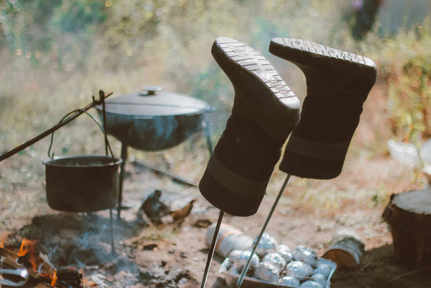 kamperen in de natuur na een wandeling, koken in een pot boven een vuur, schoenen drogen. recreatie buitenshuis. toeristische weekenden - Foto, afbeelding