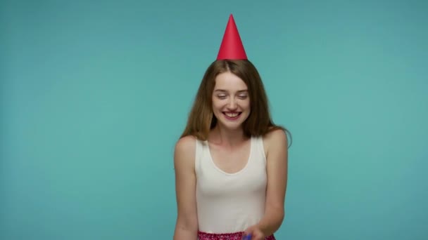 Optimistic happy girl in summer dress and funny cone on head laughing carefree, blowing party horn, celebrating birthday congratulating with holidays, festive mood. indoor studio shot isolated - Filmati, video