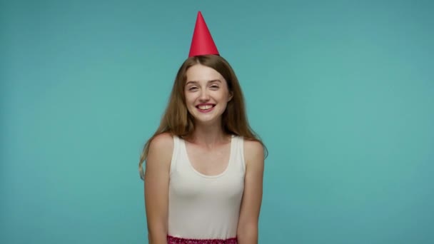 I love myself! Optimistic girl in summer dress and funny party cone on head laughing carefree, embracing herself, celebrating birthday alone and happy. indoor studio shot isolated on blue background - Imágenes, Vídeo