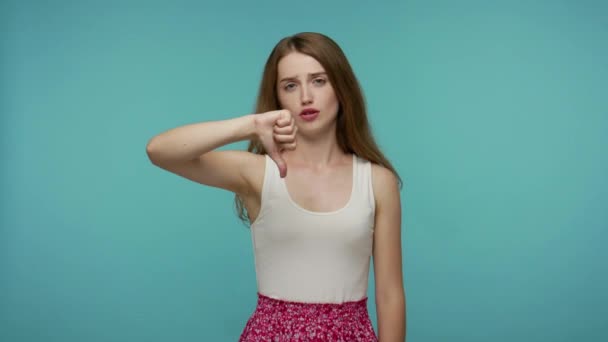 Upset disappointed girl in dress showing double thumbs down, saying No, don't like and refusing bad choice, criticizing with dislike gesture, disapproval. studio shot isolated on blue background - Πλάνα, βίντεο