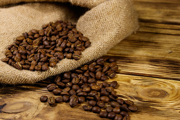 granos de café tostados en saco sobre mesa de madera - Foto, Imagen