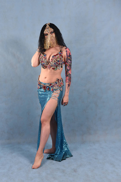 A beautiful dancer in an Oriental dress with a veil and a red skirt with full Breasts on a blue background in the Studio - Foto, immagini