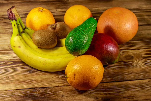 Ассортимент тропических фруктов на деревянном столе. Натюрморт с бананами, манго, апельсинами, авокадо, грейпфрутом и киви
 - Фото, изображение