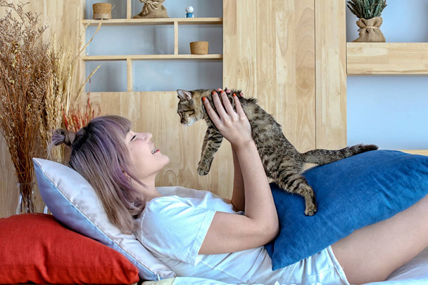 Glückliches asiatisches Mädchen, das mit Katzen auf dem Schlafsofa spielt. Asiatische Frauen spielen mit Katzen im Wohnzimmer. - Foto, Bild