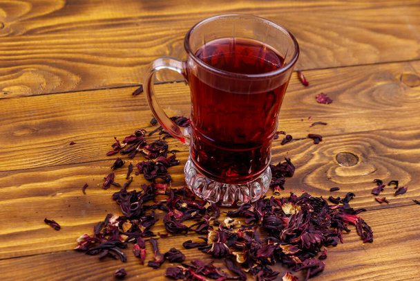 Γυάλινο φλιτζάνι κόκκινο τσάι ιβίσκου (καρκέιντ, ροδοσέλ) σε ξύλινο τραπέζι - Φωτογραφία, εικόνα