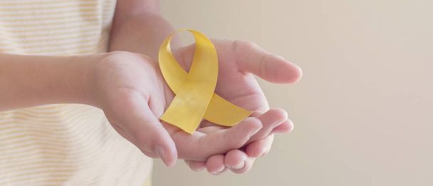 Hands holding yellow gold ribbon, Sarcoma Awareness, Bone cancer, childhood cancer awareness, September yellow, World Suicide Prevention Day concept - Fotografie, Obrázek