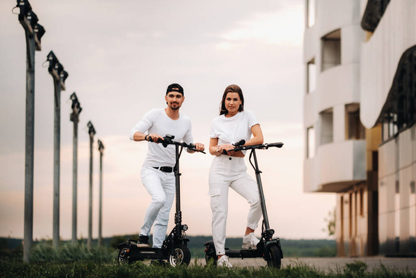 A girl and a guy are walking on electric scooters around the city, a couple in love on scooters - Fotoğraf, Görsel