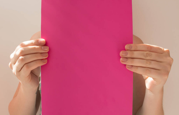 Hands of young woman holding blank pink sheet of paper for text and design, mock up on light background. Minimal concept. - Фото, изображение
