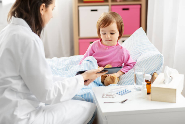 doctor with tablet computer and sick girl in bed - Fotoğraf, Görsel