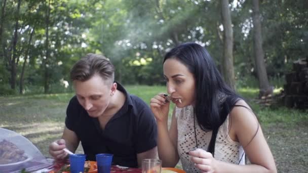 A handsome guy and a beautiful girl eat in nature, laugh at each other - Materiał filmowy, wideo