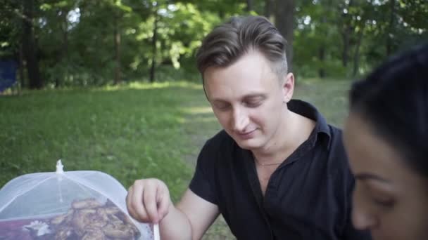 A handsome guy and a beautiful girl eat in nature, laugh at each other - Filmmaterial, Video
