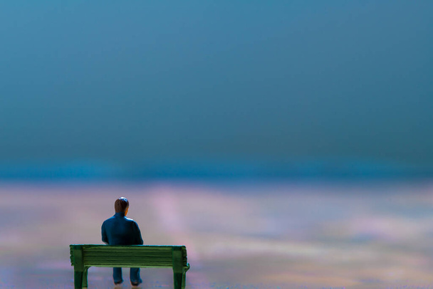 Miniatyyri hahmo poseeraa kuin mies istuu yksin penkillä surrealistisessa maisemassa, minimalistinen abstrakti konsepti kuva - Valokuva, kuva