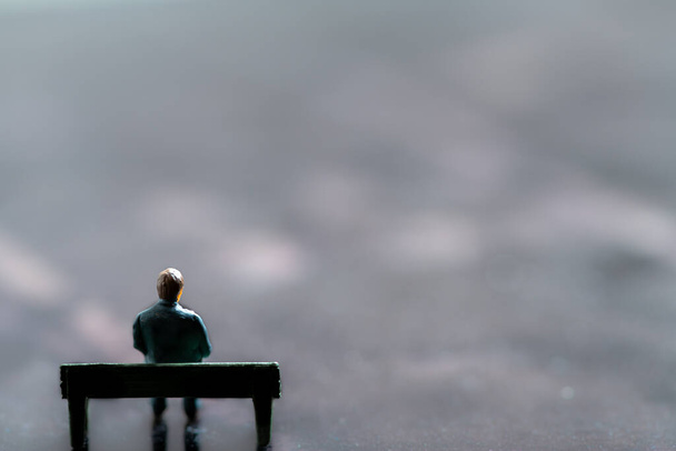 Miniatuur beeldje dat zich voordeed als man die alleen op een bankje zat in surrealistisch landschap, minimalistisch abstract concept beeld - Foto, afbeelding