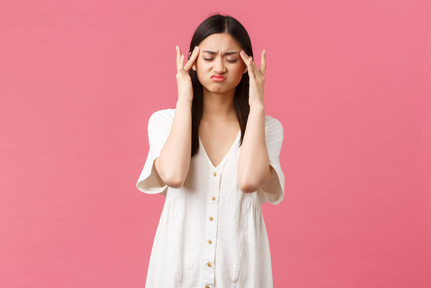 Beauty, people emotions and summer leisure and vacation concept. Distressed asian woman touching temples and grimacing with closed eyes from migraine, painful headache, pink background - Photo, Image