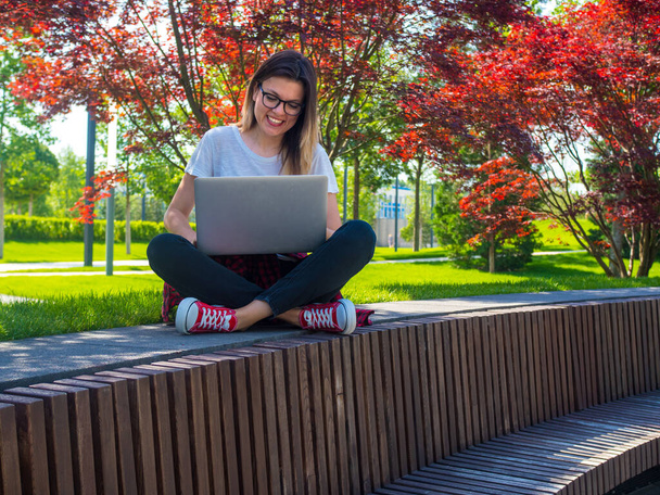 Glückliche Frau mit Brille, die im Schneidersitz mit Laptop im Freien sitzt. Online-Bildung - Foto, Bild