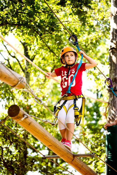 Little brave caucasian girl at outdoor treetop climbing adventure park. 7 years old girlie climbing in a rope playground structure in 5 meters high altitude - Photo, Image