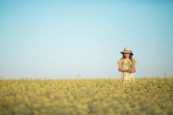portret van een mooie tiener meisje in een hoed in een geel veld tegen de hemel - Foto, afbeelding