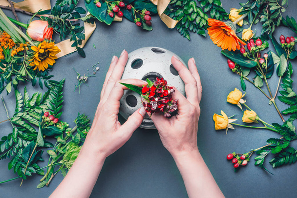Female hands make Creative autumn floral arrangement with various flowers and plant leaves arrangement on blue table , top view. Florist workplace. Greeting and holiday, concept - Foto, Bild