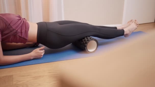 Νεαρή Ασιάτισσα γυμνασμένη και σταθερή γυναίκα που κάνει μασάζ στα πόδια της χρησιμοποιώντας αφρό κυλώντας στο yoga matt μέσα στο σαλόνι το Σαββατοκύριακο, υγειονομική περίθαλψη και εναλλακτική θεραπεία, αποκατάσταση στην αθλητική ιατρική - Πλάνα, βίντεο