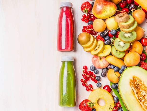 Red and green smoothies and juices beverages in bottles with various fresh organic fruits and berries ingredients on white wooden background, top view. Healthy food and vegetarian concept - Photo, Image