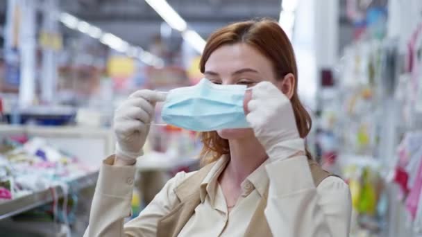 retail, pretty girl shopper in gloves puts a mask on his face to protect against coronavirus while shopping on childrens clothing - Кадры, видео