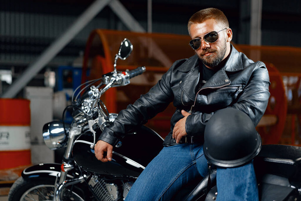 Portrait of bearded man motocyclist in dark sunglasses on dark background - Zdjęcie, obraz