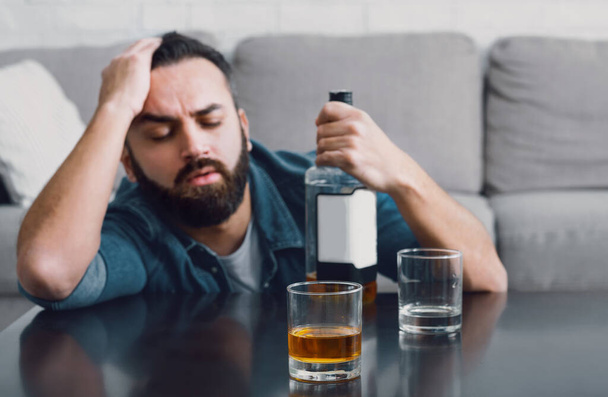 Depressie en alcoholisme thuis. Man valt in slaap en houdt fles vast - Foto, afbeelding