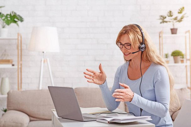 Ondersteuning en online consultatie vanuit huis. Vrouw met headset werkt op afstand op laptop - Foto, afbeelding