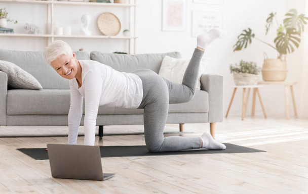 Fitness zu Hause. Sportliche Seniorin turnt vor Laptop - Foto, Bild