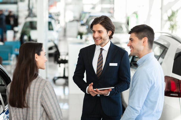Salesman Offering Couple Car Standing In Auto Showroom - Foto, imagen