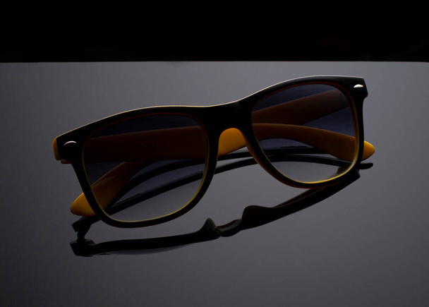 Detailní záběr žluté s černými slunečními brýlemi na šedém pozadí. - Fotografie, Obrázek