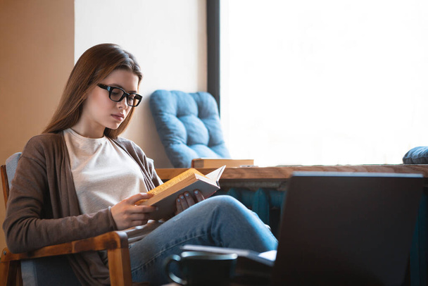 Young woman reads interesting book and sits at home - Foto, imagen