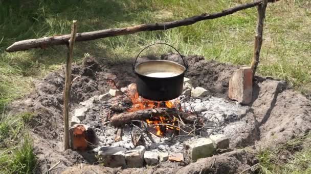 観光客はたき火の上にホイストボウラー帽子を吸っていました。キャンプの朝食が用意されています. - 映像、動画