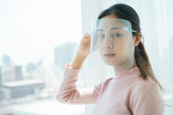 New normal fashion - Asian thai long dark hair woman wearing face shield stay home in apartment. - Photo, Image
