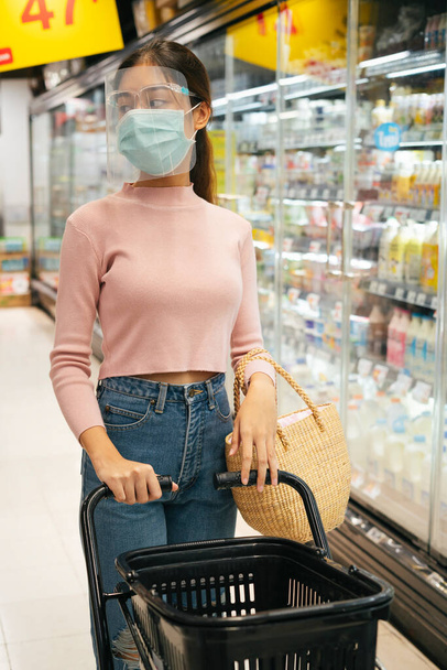 Новая нормальная жизнь - азиатская тайская женщина в маске и маске за покупками в супермаркете
. - Фото, изображение