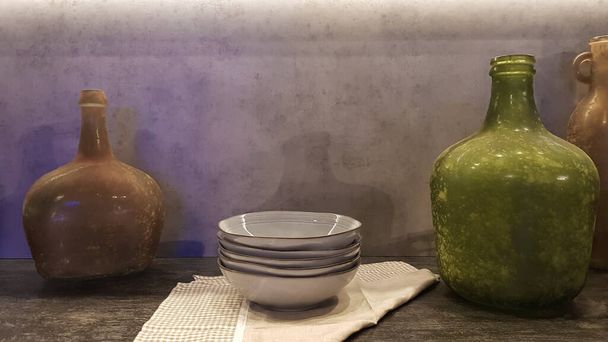 Великі скляні вази, кошик з яблуками і тарілками в інтер'єрі сучасної кухні. Поєднання дерева і бетону в дизайні. Сучасний стиль їдальні кухні
. - Фото, зображення
